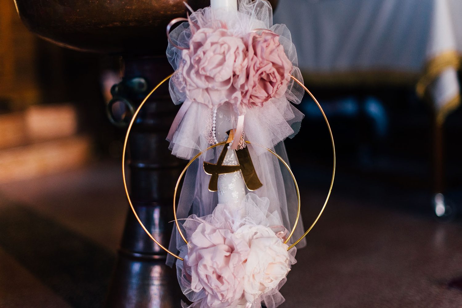 Decorated christening candle with pink fabric flowers, tulle, and a gold letter A inside gold rings