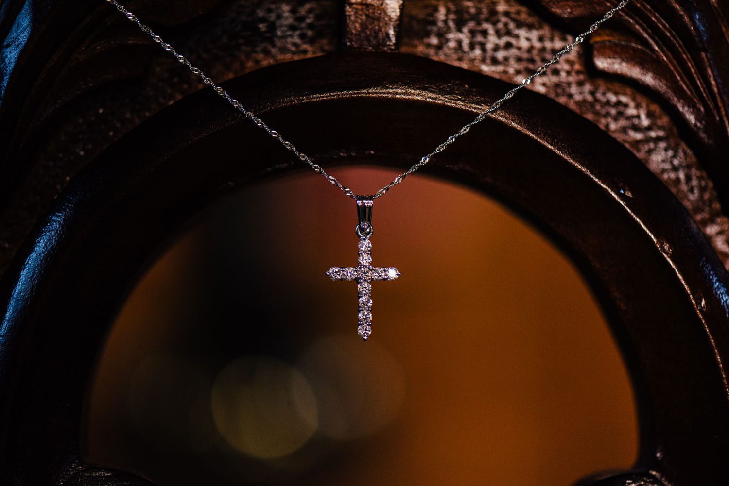 Diamond cross necklace hanging in front of the carved wooden baptism font