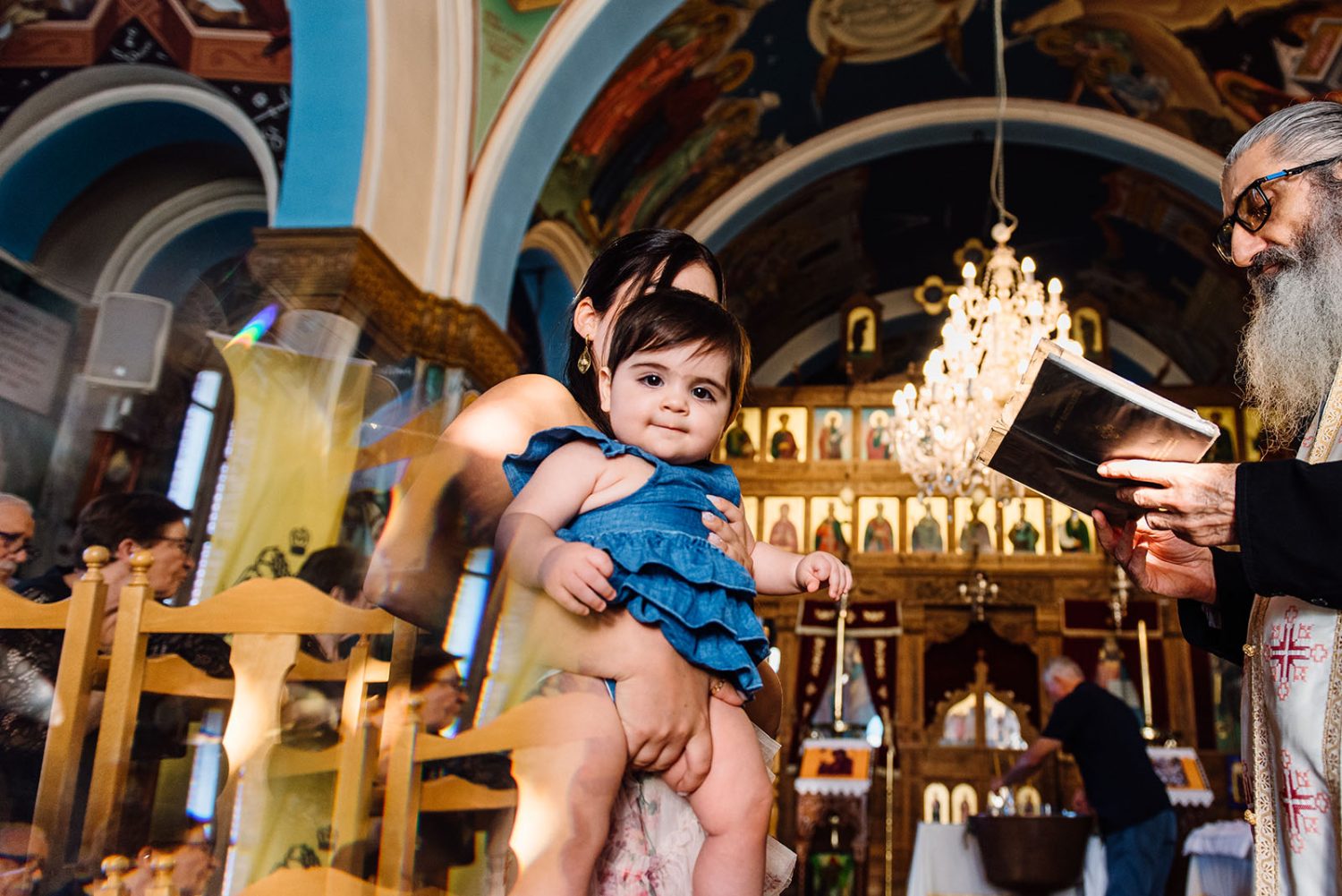 Godmother holding the baby girl in a blue dress inside a church while the priest reads from a book