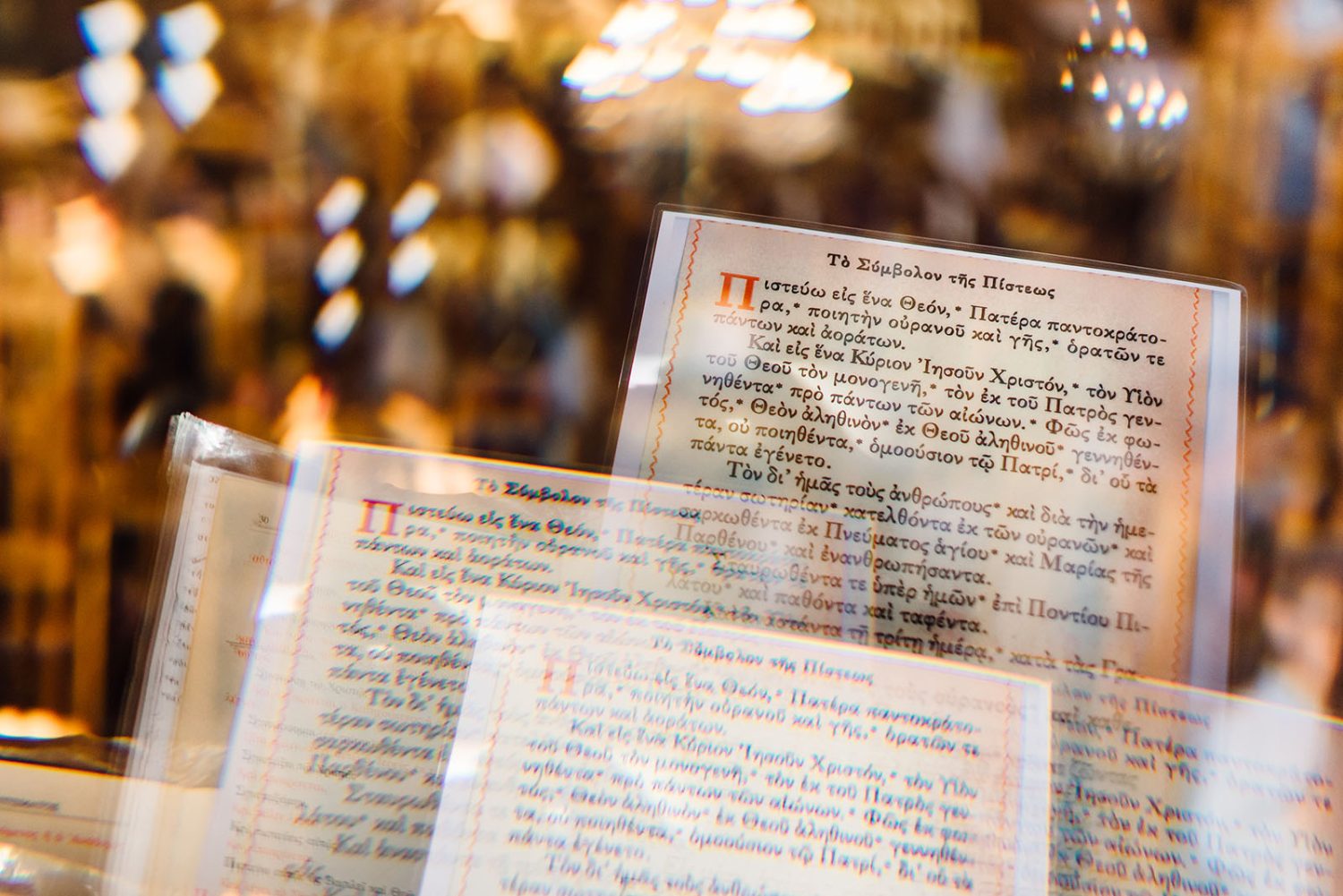 Greek Orthodox prayer texts on printed cards in a church, with warm blurred lights behind