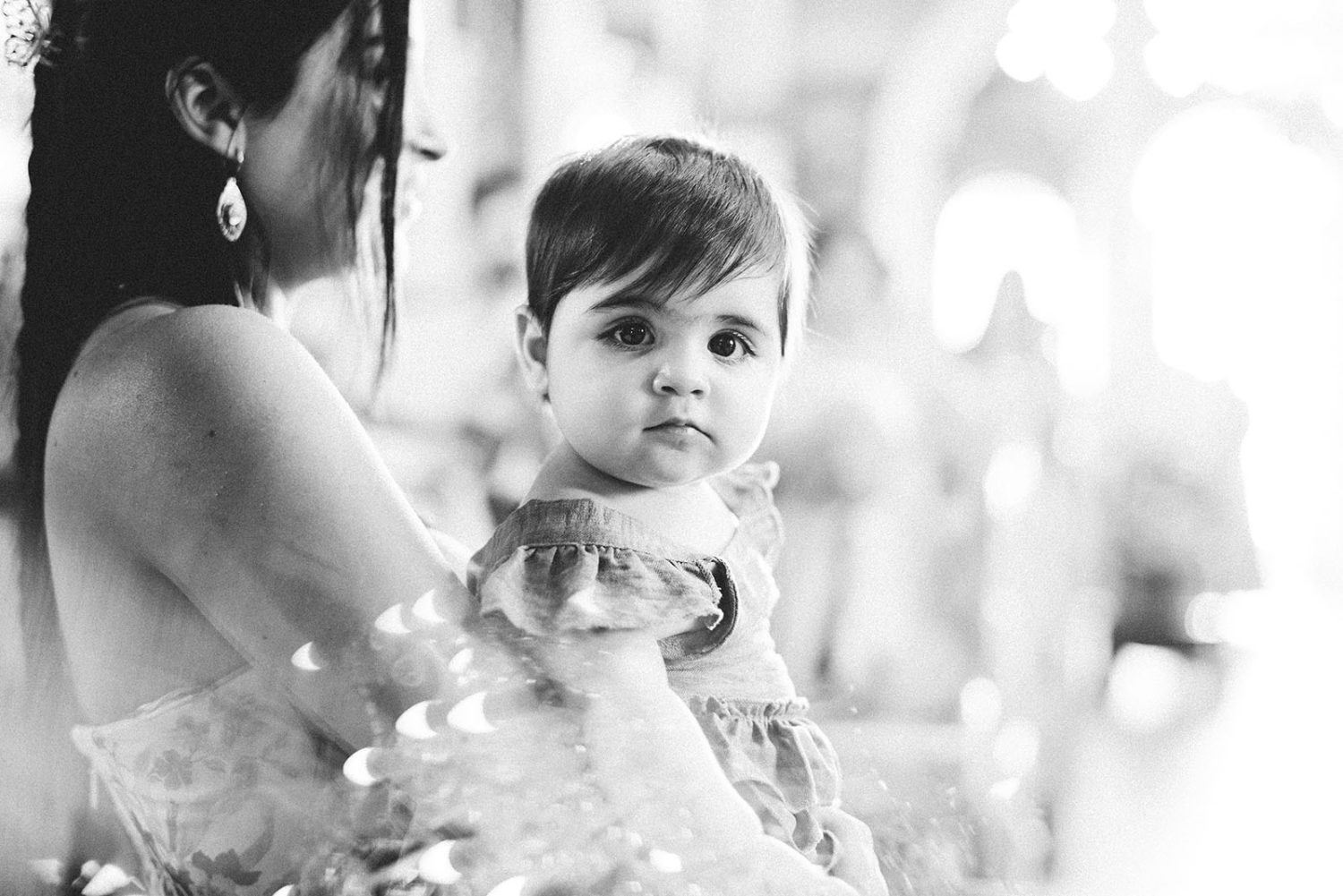 Black and white close-up of the baby girl looking at the camera, held by the godmother in church