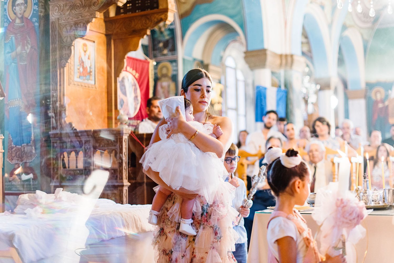 Godmother carrying the baby girl in a white tulle dress through the church, with guests behind