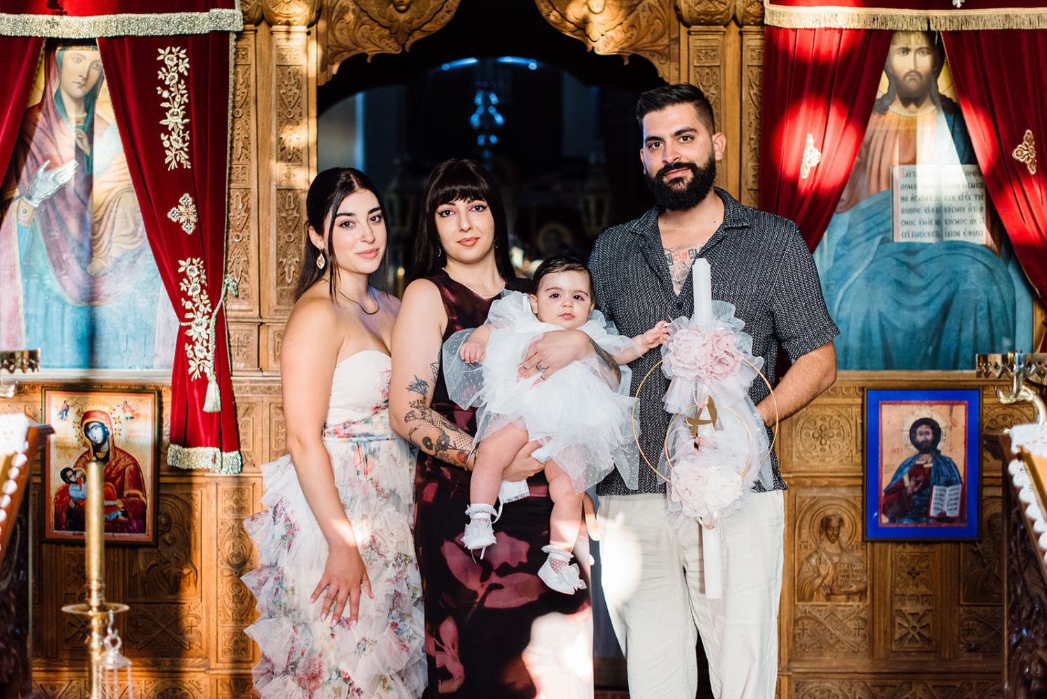 Family portrait in front of the church iconostasis, with the baby girl in white and a decorated candle